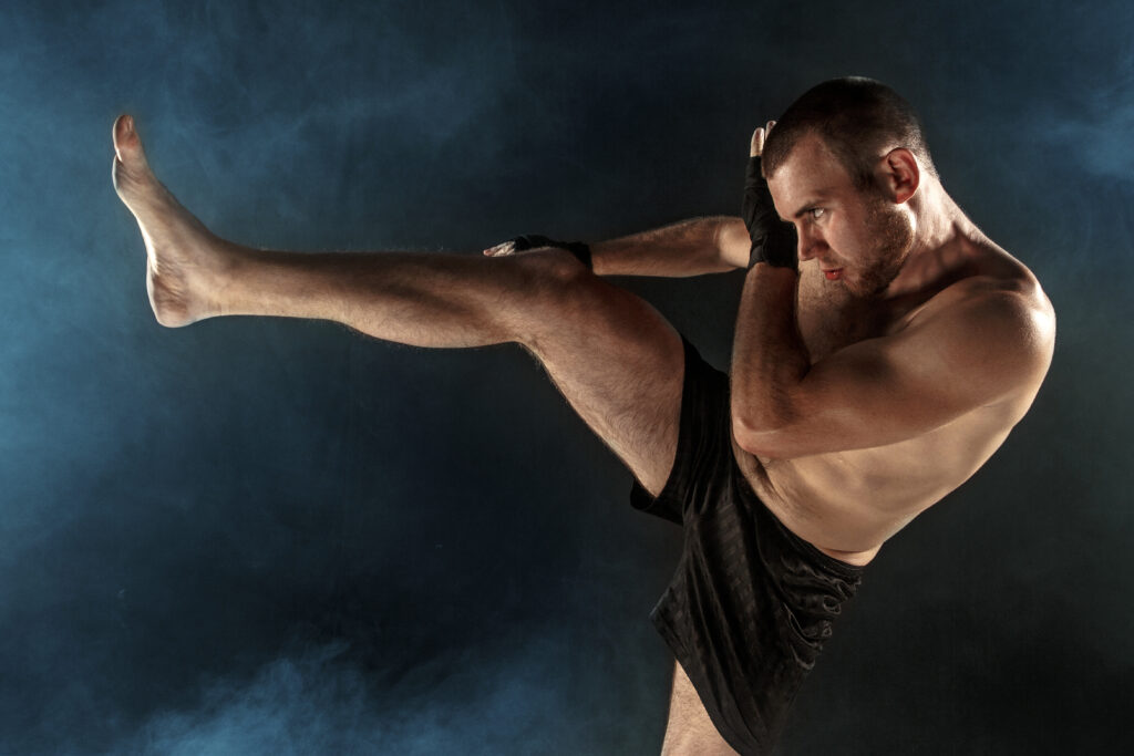 The young male athlete kickboxing on a black background